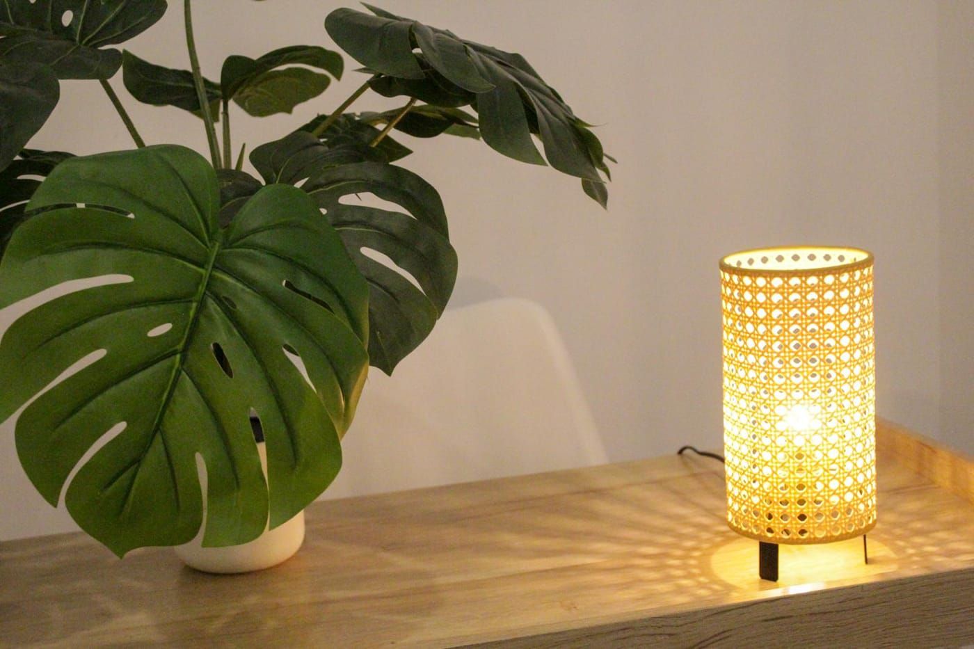 Lámpara de mimbre encendida sobre un taburete de madera en la consulta de PsicoDiversa, entre plantas y luz cálida